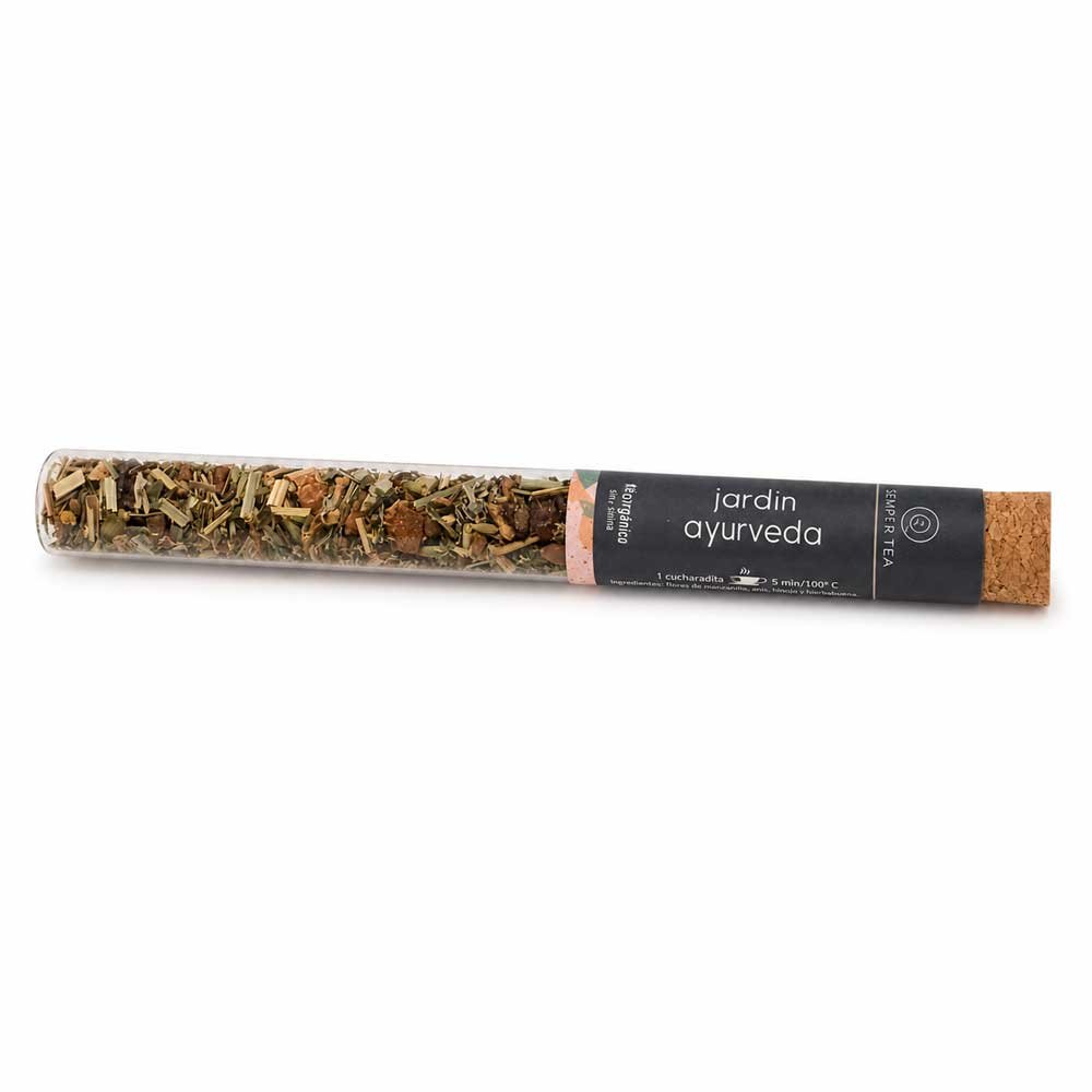 Imagen de Jardín Ayurveda en tubo de cristal con taza de infusión al fondo. Una presentación elegante, natural y perfecta como regalo wellness o detalle gourmet.